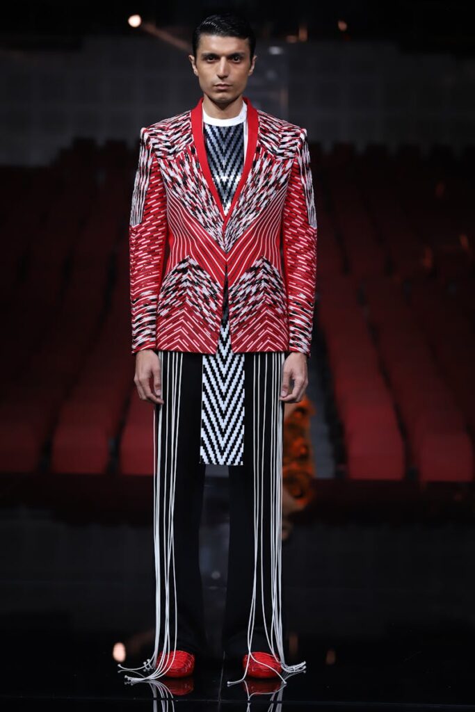 A model showcases a vivid, patterned red and black suit on a catwalk in New Delhi.