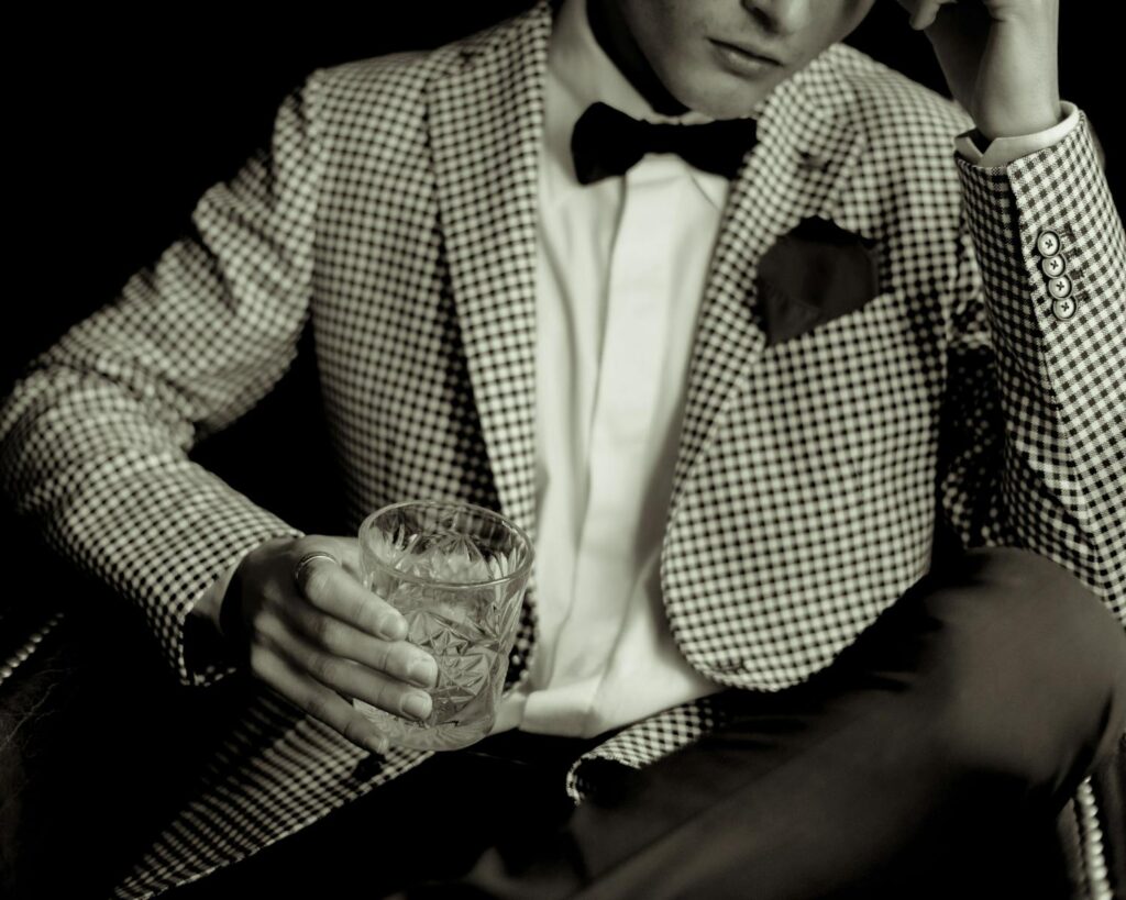 Stylish man in an unusual houndstooth mens suit jacket holding whisky, embodying luxury and elegance.