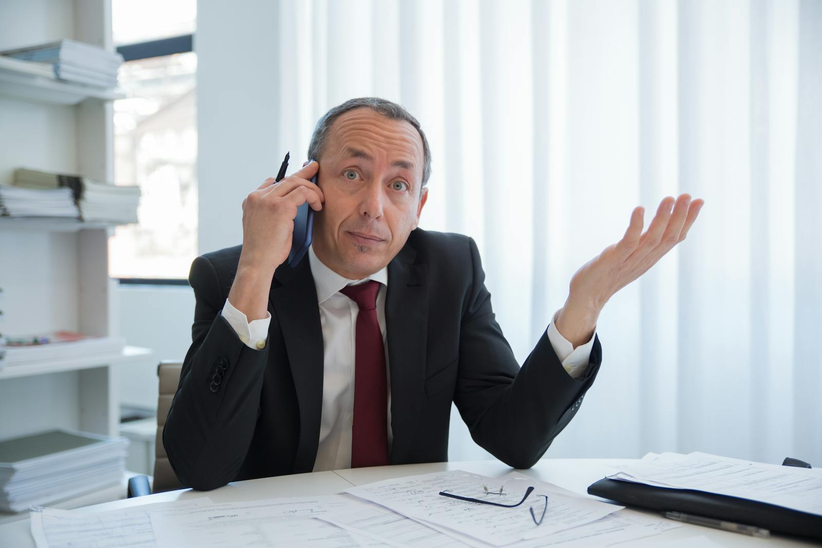 Business professional in a suit talks on the phone while gesturing in an office.