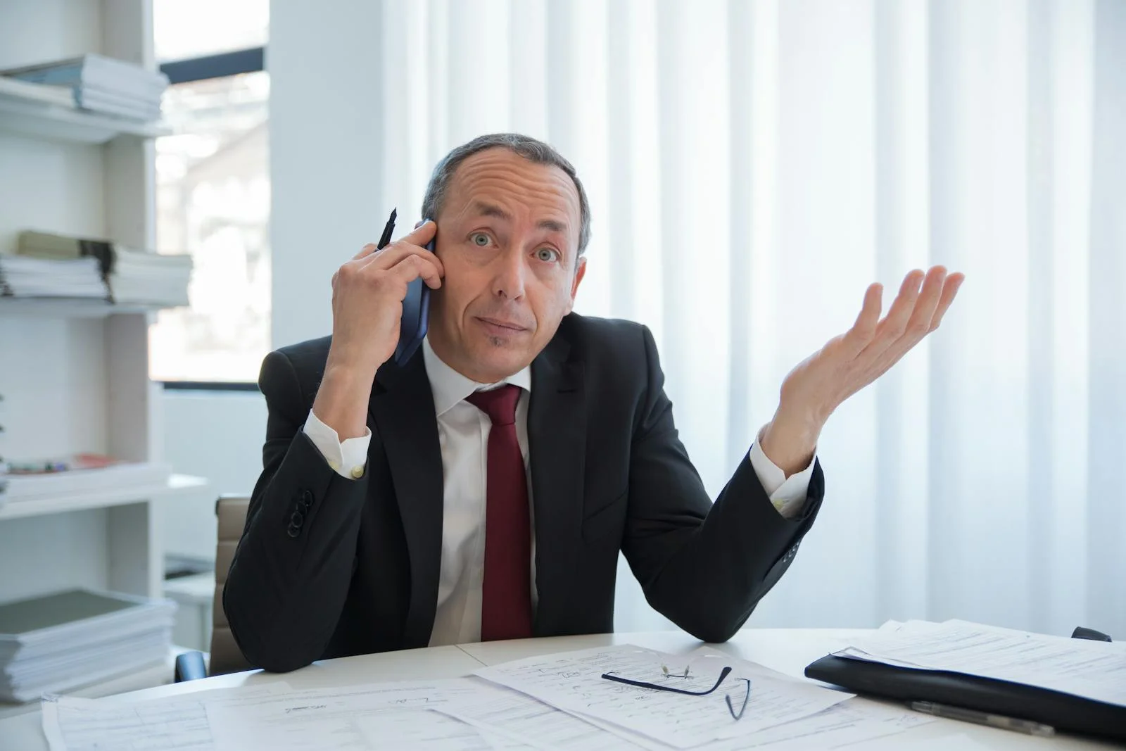 Photo by Kampus Production Business professional in a suit talks on the phone while gesturing in an office.